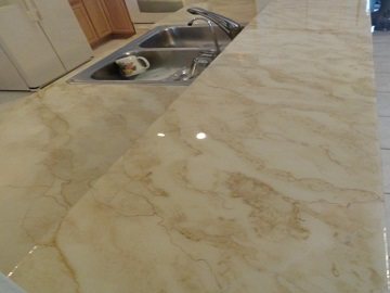 A kitchen countertop finished in pale cream concrete with soft tan veining, running up to a stainless steel double sink.