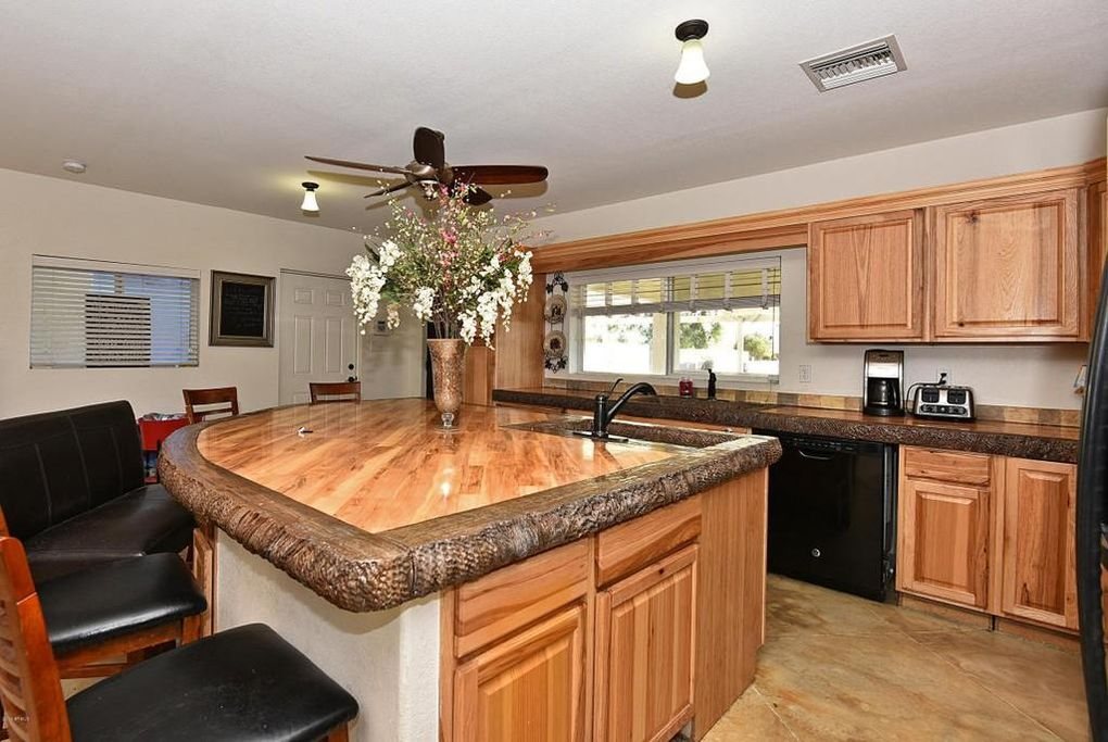 A large kitchen island with a concrete countertop finished to look like wide timber planks, edged with a heavily chiselled dark stone border, in a kitchen with hickory cabinets.