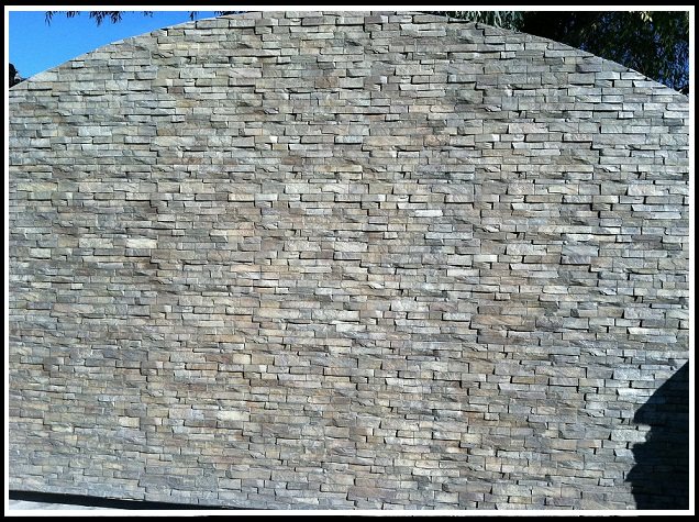 A tall gated backyard entry with an arched top, clad entirely in pale grey and tan stacked stone panels.