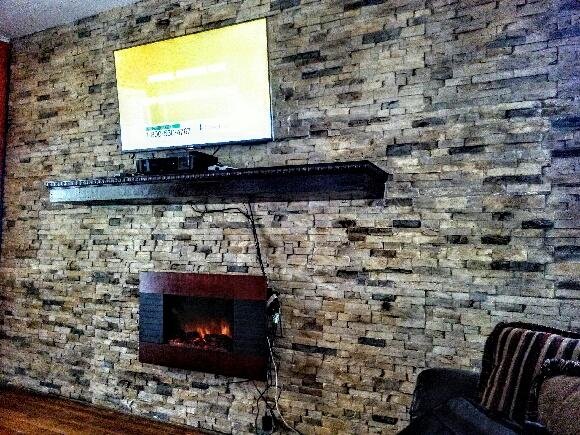 A living room feature wall clad in SBC stone panels around a television.